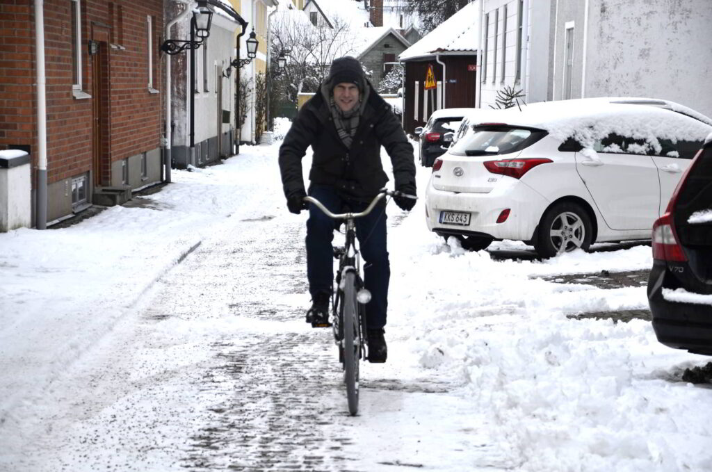 Cykeln som symbol. Bild på cyklande man bland parkerade bilar. 